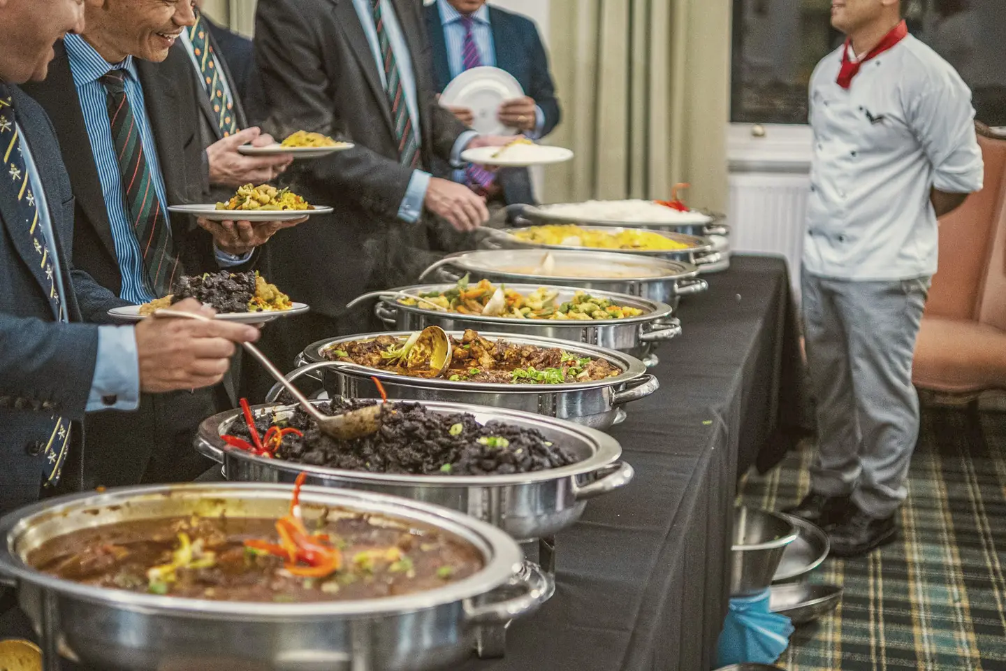 Guests in business dress at a Unique House buffet line with a server standing by