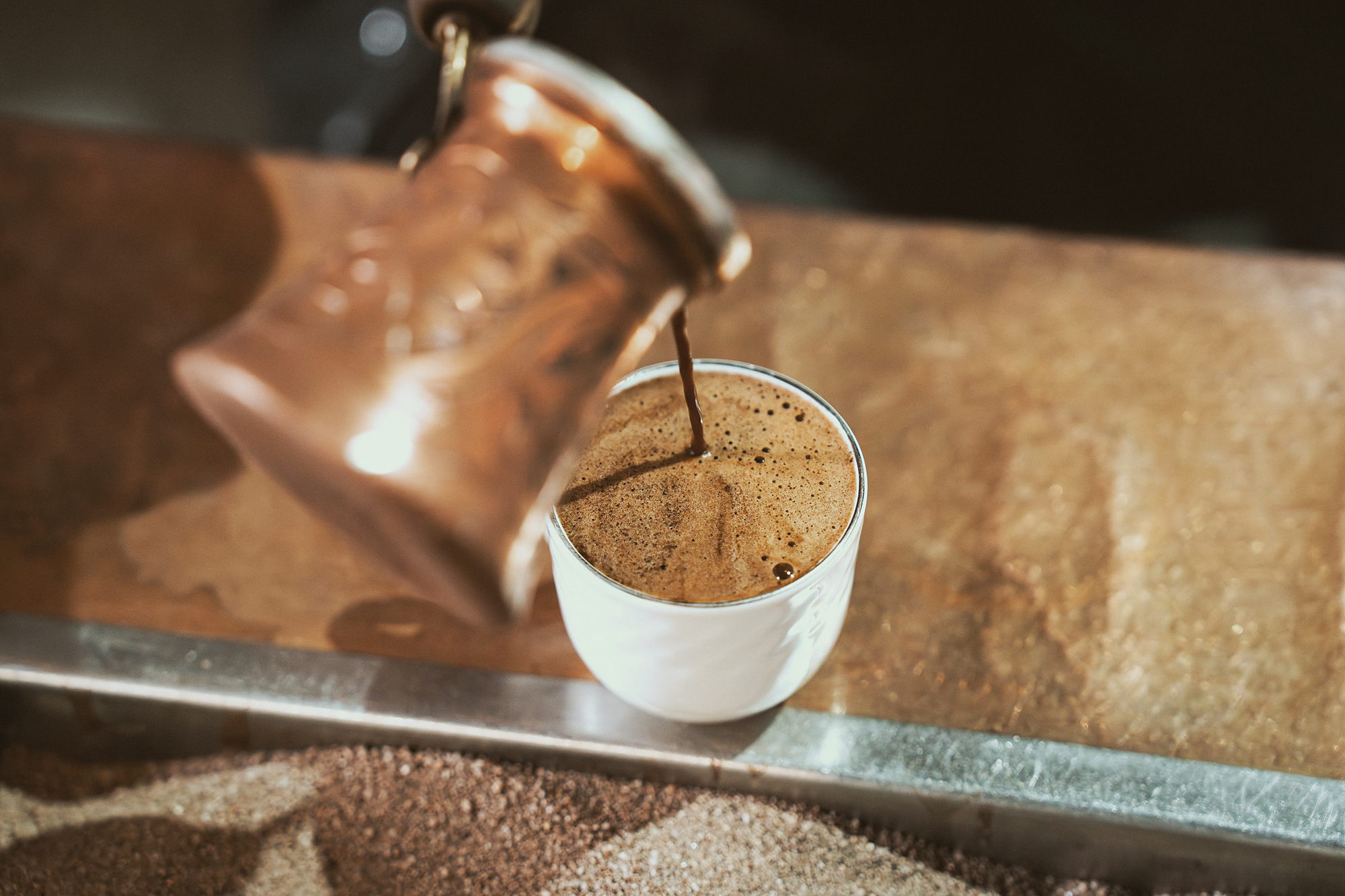 Coffee poured from a copper pot into a white cup